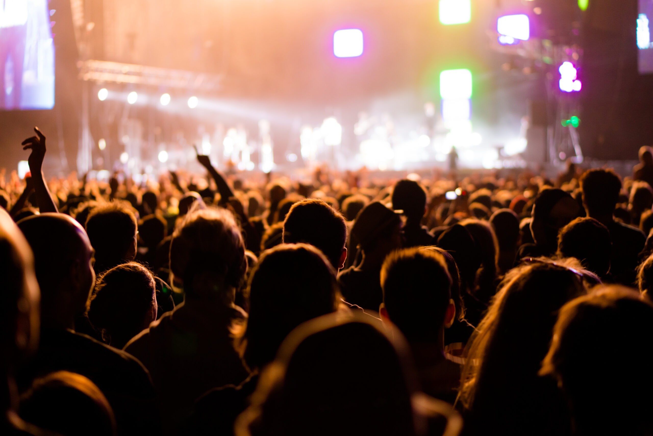 A vibrant crowd at a concert, with raised hands and colorful stage lights, captures the energy of a live music event.