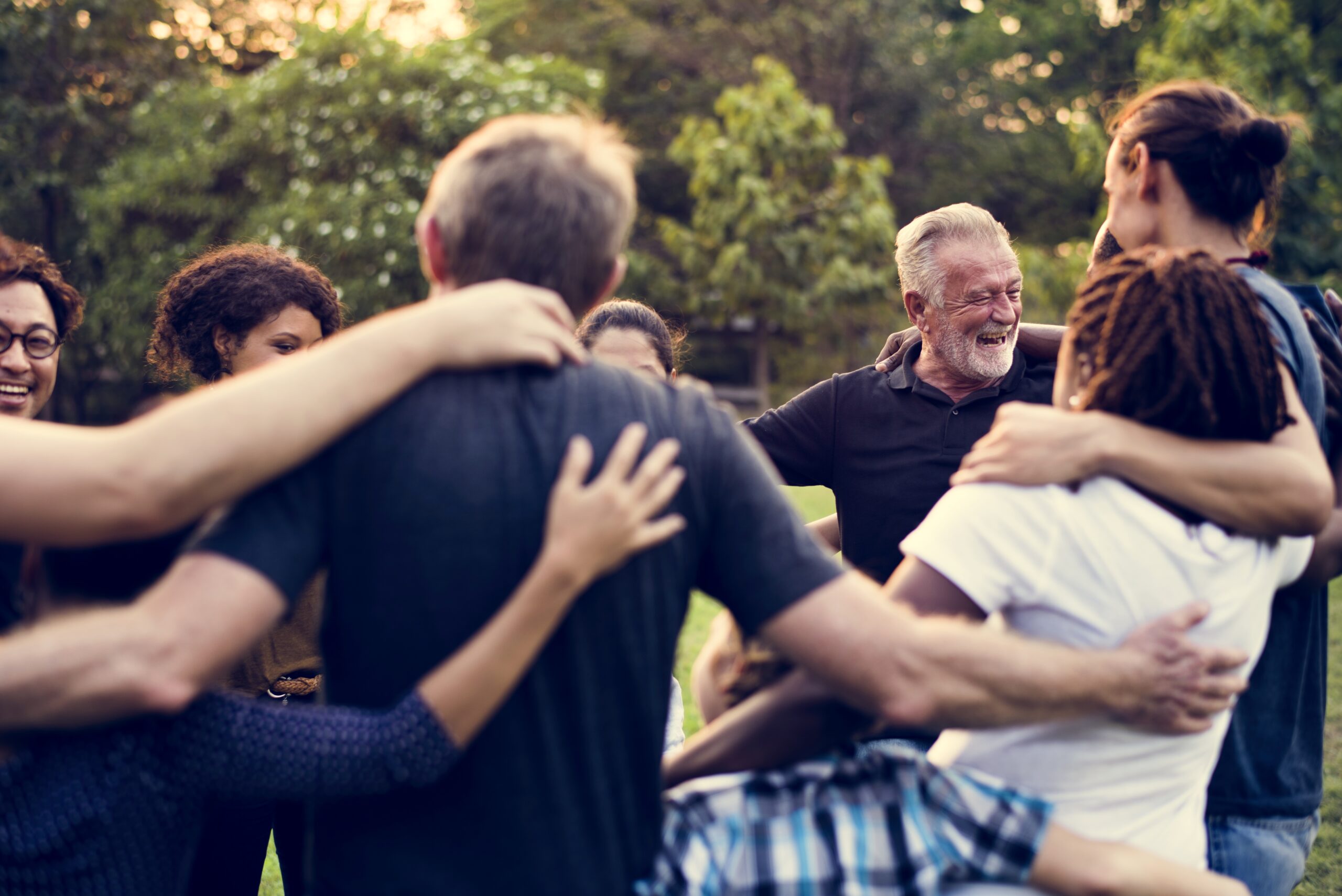 A diverse group of people joyfully embracing in a circle outdoors, sharing laughter and smiles, symbolizing community and connection.